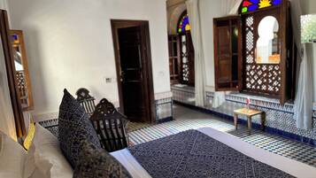 A traditional Moroccan room with a patterned bed, a wooden chair, and a small table.