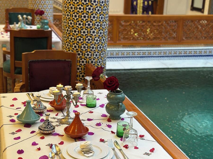 Una mesa de comedor decorada con elementos tradicionales marroquíes, incluyendo una tetera, una jarra y un florero con una rosa.