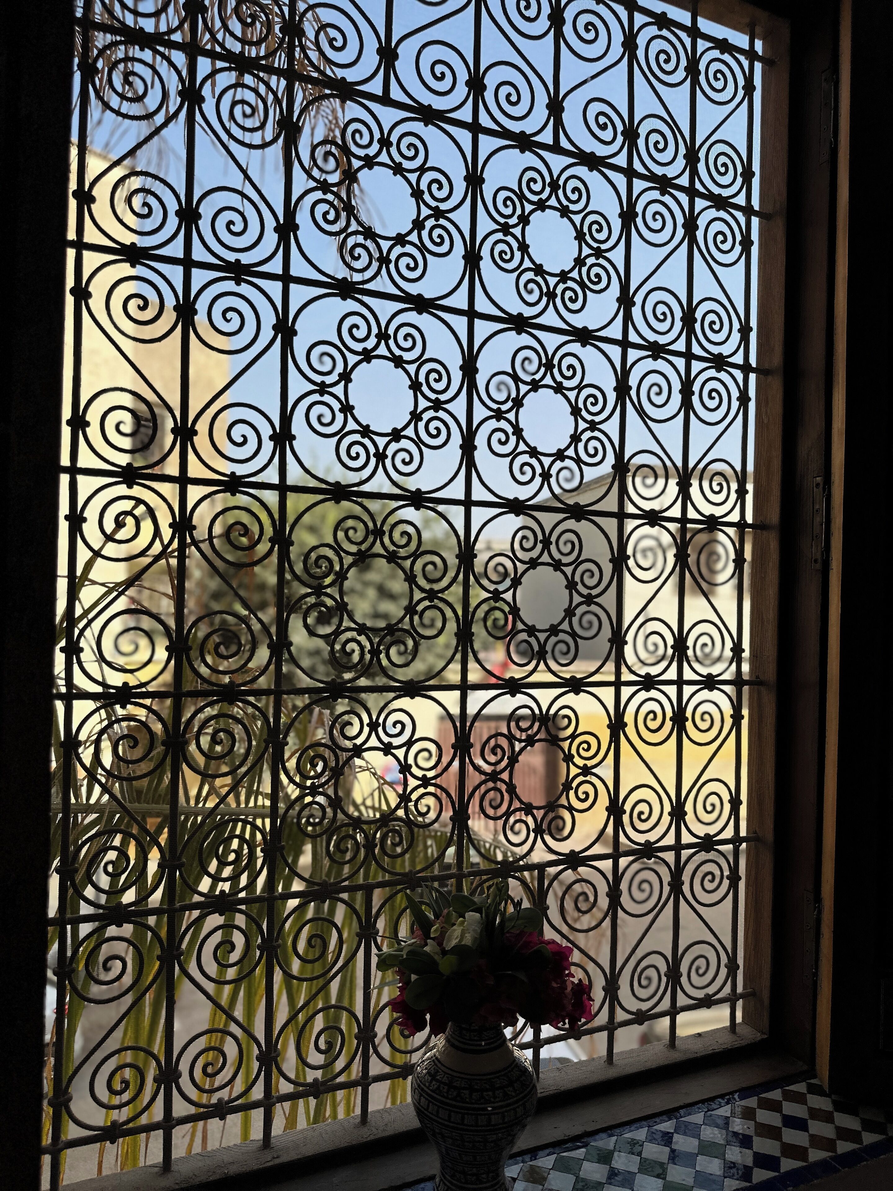 Una ventana con intrincados detalles de hierro forjado y un florero con flores.