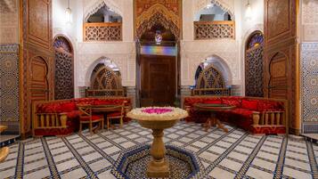 An ornate interior with a central fountain, red cushioned seating, and intricate tile work.