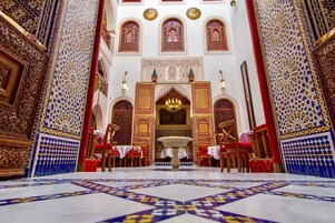 Un interior ornamentado con detalles intrincados en azulejos, una lámpara central y una disposición simétrica con muebles rojos y blancos.
