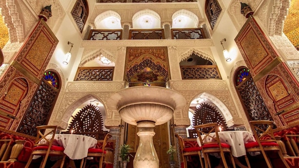 Un salón imponente con arcos decorativos, una fuente central y arreglos para sentarse.
