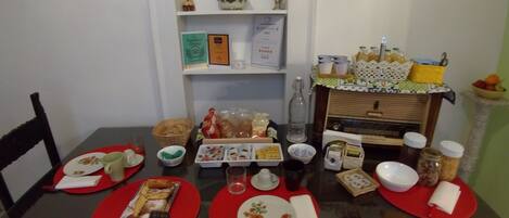 A dining table set with red placemats, plates, and various food items. There are shelves with decorative items and a small table with drinks and snacks.
