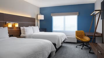 A hotel room with two beds, a desk, a chair, a large window, and a wall-mounted TV.
