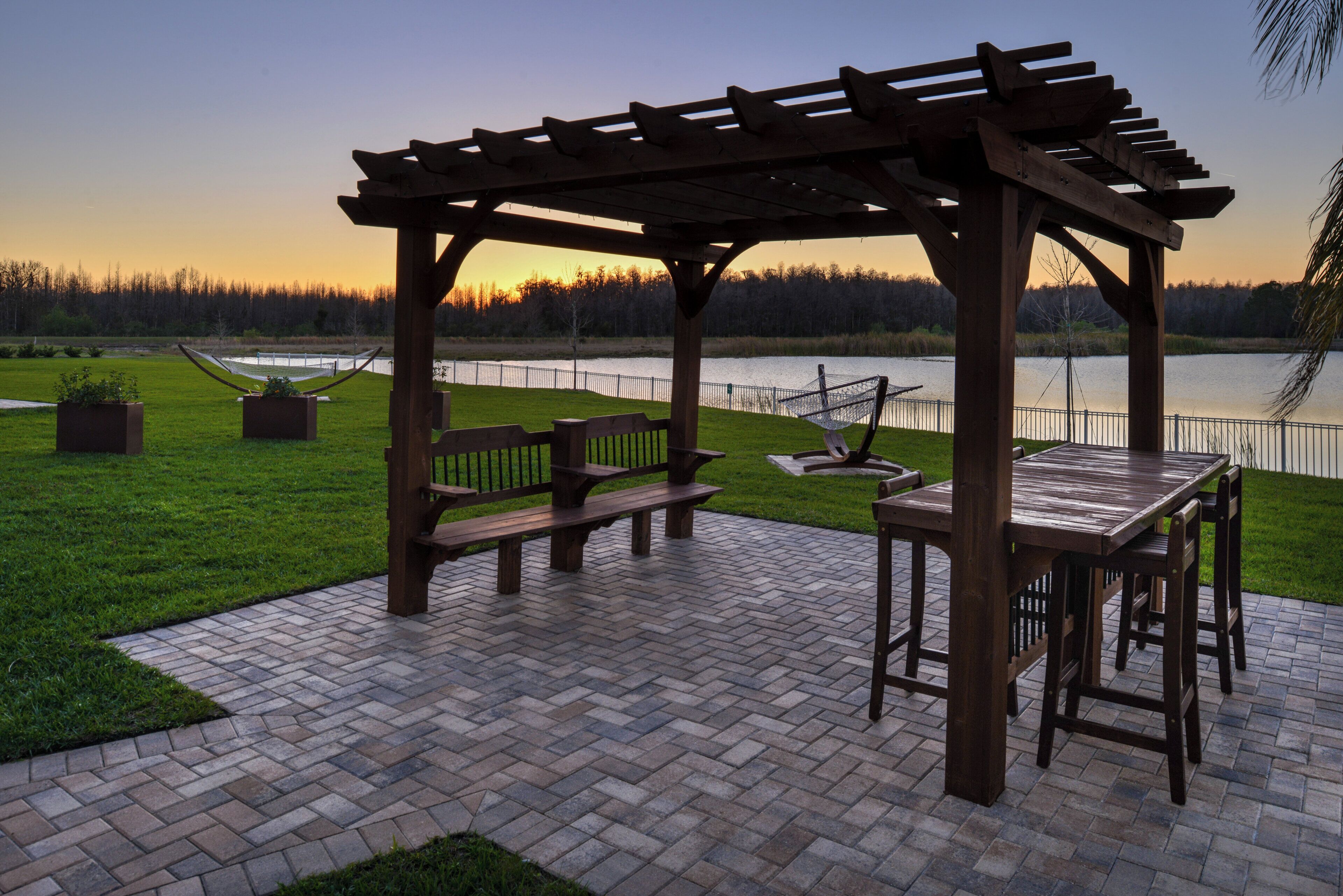 A wooden pergola with benches and a table, overlooking a body of water.