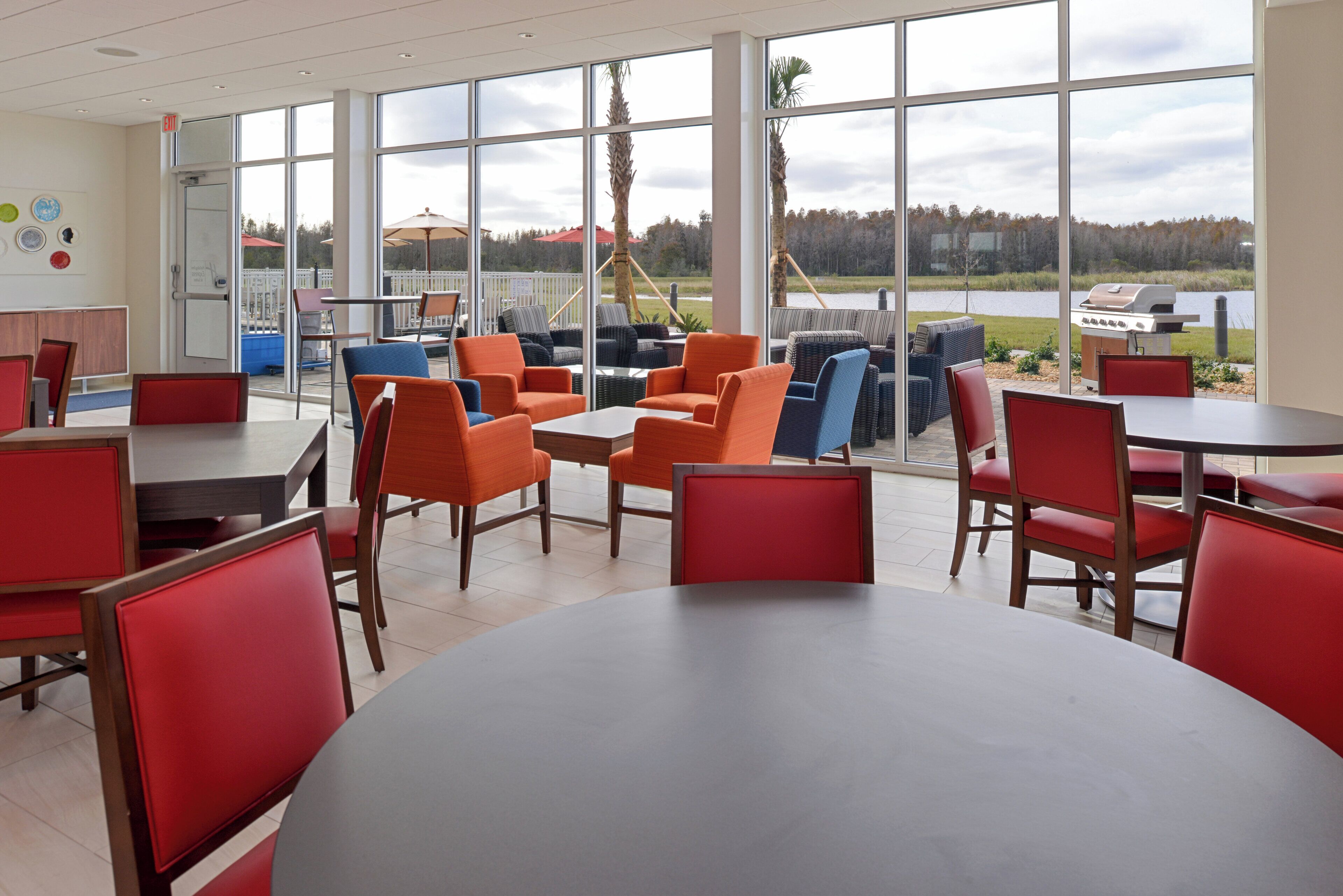 A restaurant with large windows, red and blue chairs, and a view of a lake.