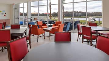 A restaurant with large windows, red and blue chairs, and a view of a lake.