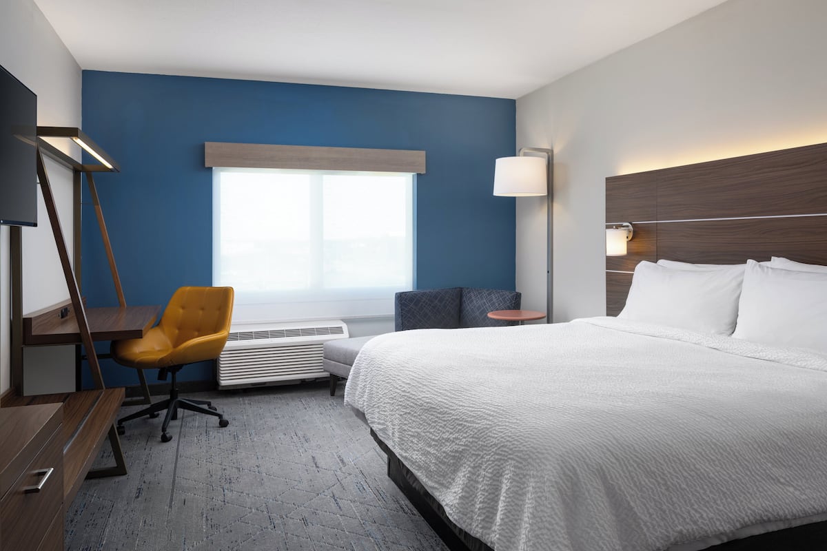A hotel room with a bed, a desk, a chair, a lamp, and a window.