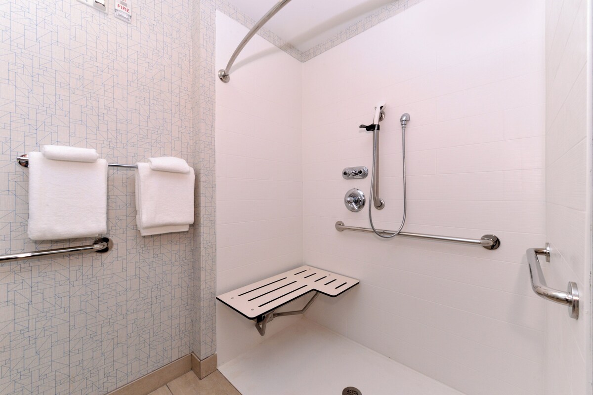 A bathroom with white tiled walls, a shower with a grab bar, and two white towels on a rack.