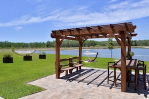 A wooden pergola with benches and a table, overlooking a body of water.