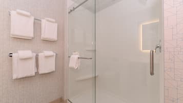Un baño moderno con cabina de ducha de vidrio, múltiples toallas blancas en un perchero y un revestimiento de pared con estampado geométrico.
