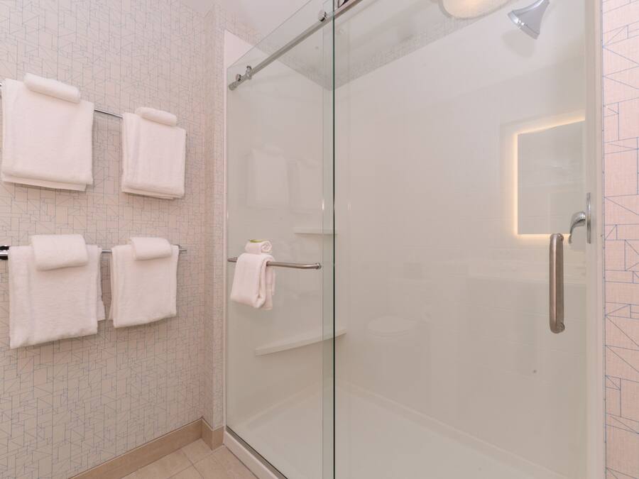 A modern bathroom with a glass shower enclosure, multiple white towels on a rack, and a geometric patterned wall.