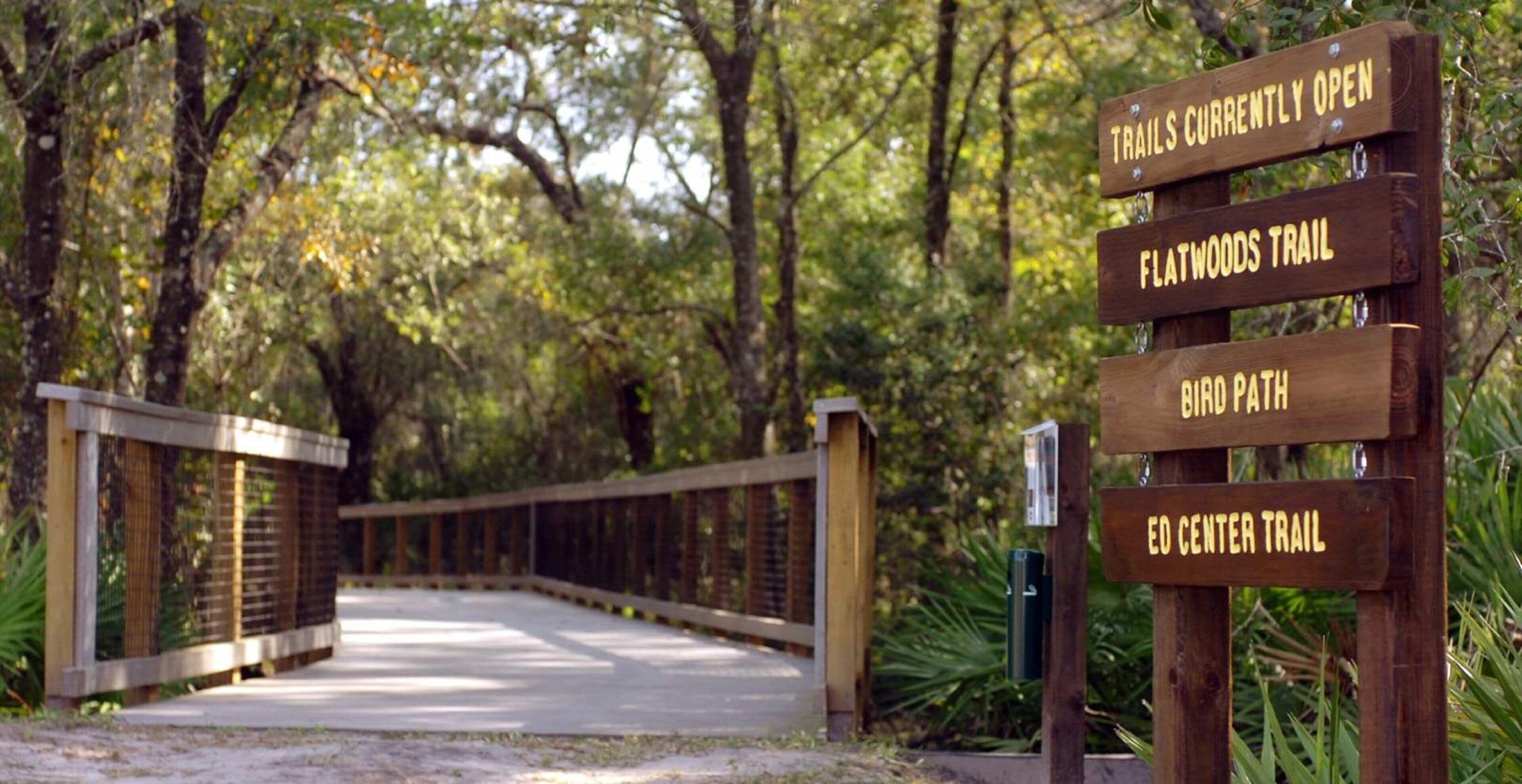 Un panneau indicateur en bois, doté de plusieurs flèches indiquant différentes directions et signalant des sentiers tels que le « sentier de Flatwoods » et le « sentier des oiseaux ».