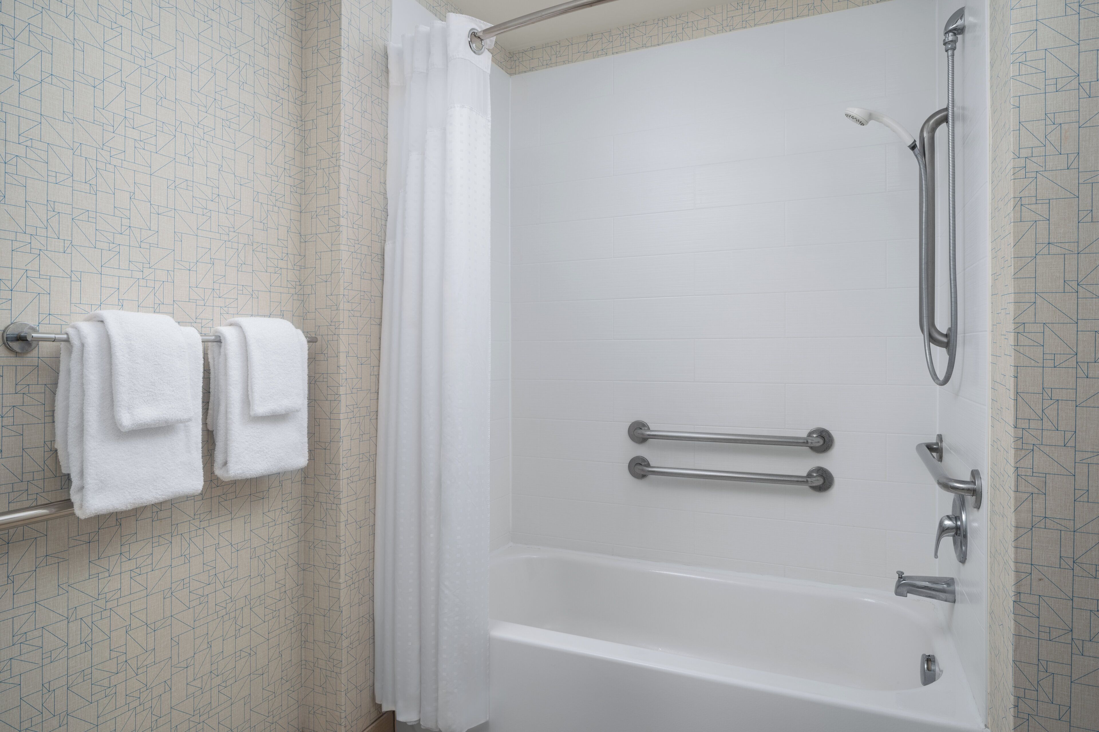 Un baño con bañera, barras de apoyo y cabezal de ducha.