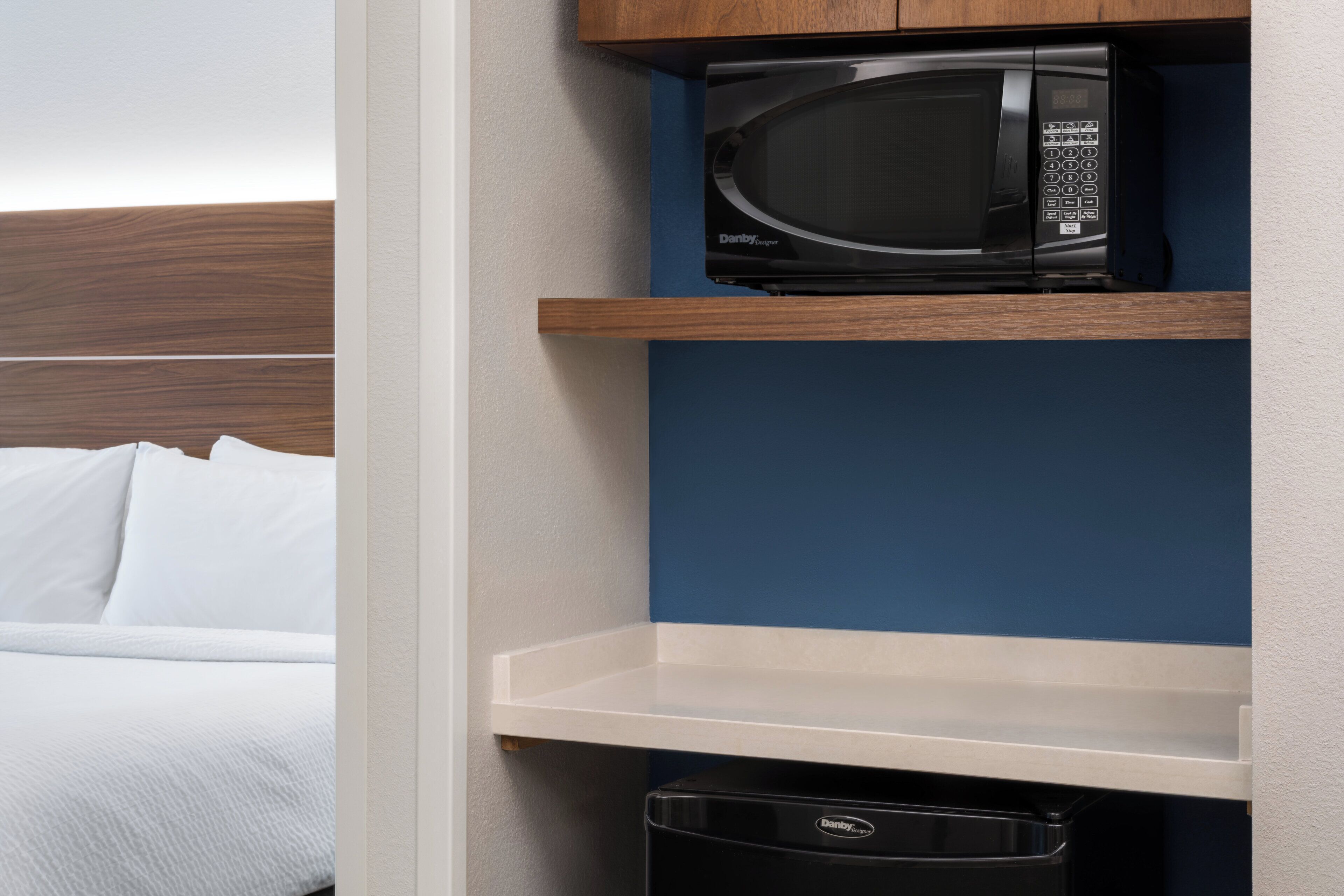 Una habitación de hotel con una cama, un microondas en un estante y un cubo de basura.