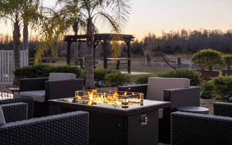 An outdoor seating area with wicker furniture and a glass-top table with a fire feature.