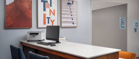 A modern office space with a white desk, two blue chairs, and framed artwork on the wall.