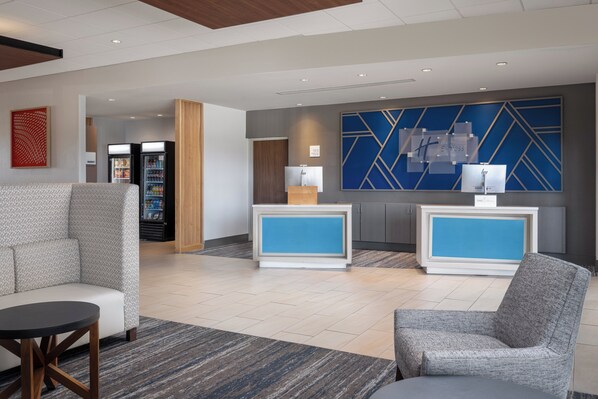 A modern lobby with seating areas, a reception desk, and vending machines. - Holiday Inn Express & Suites Trinity by IHG (Trinity)