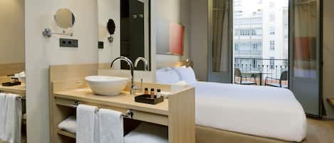 Habitación de hotel con una cama grande, lavamanos doble y balcón con vista a la ciudad.
