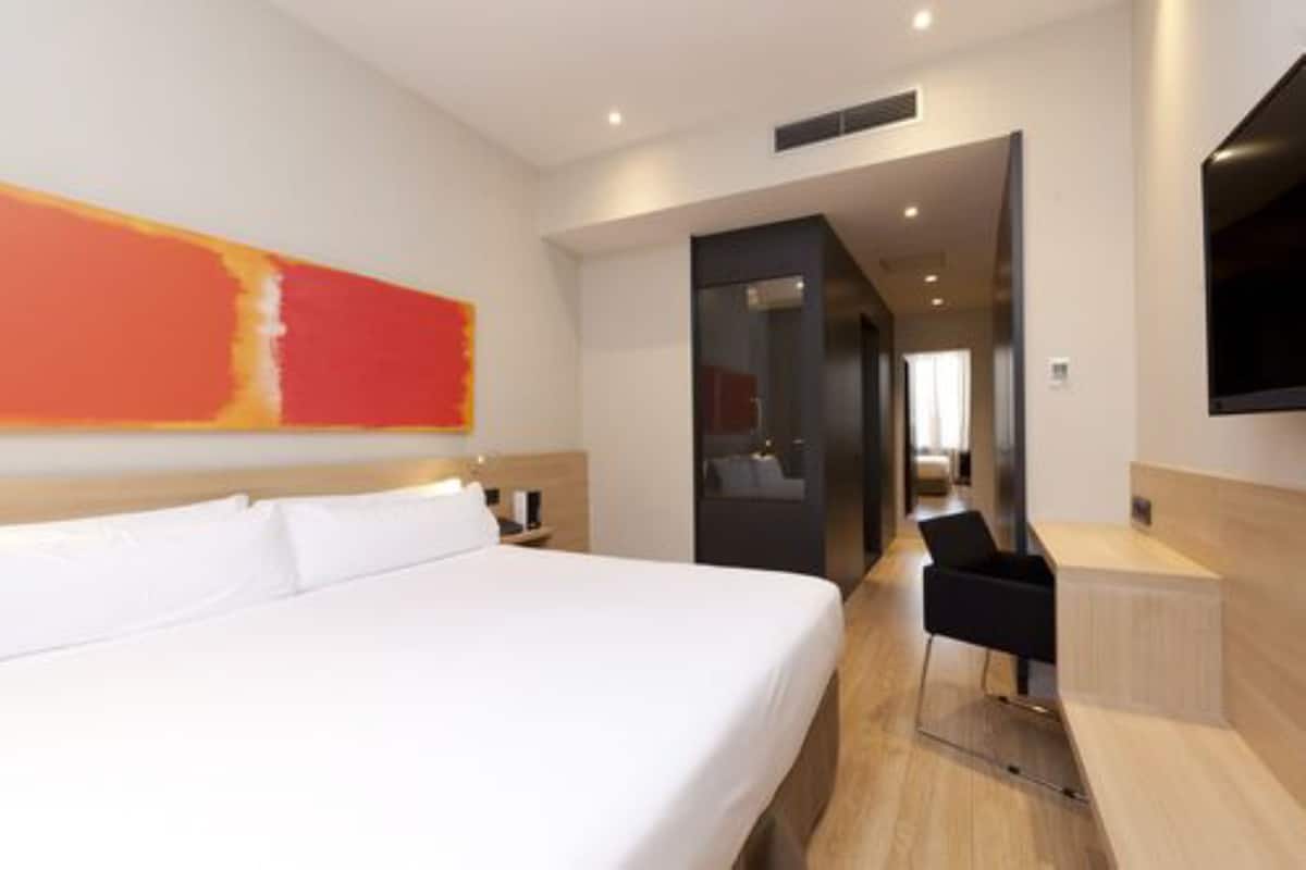 Una habitación de hotel moderna con una cama grande, un escritorio y un televisor.