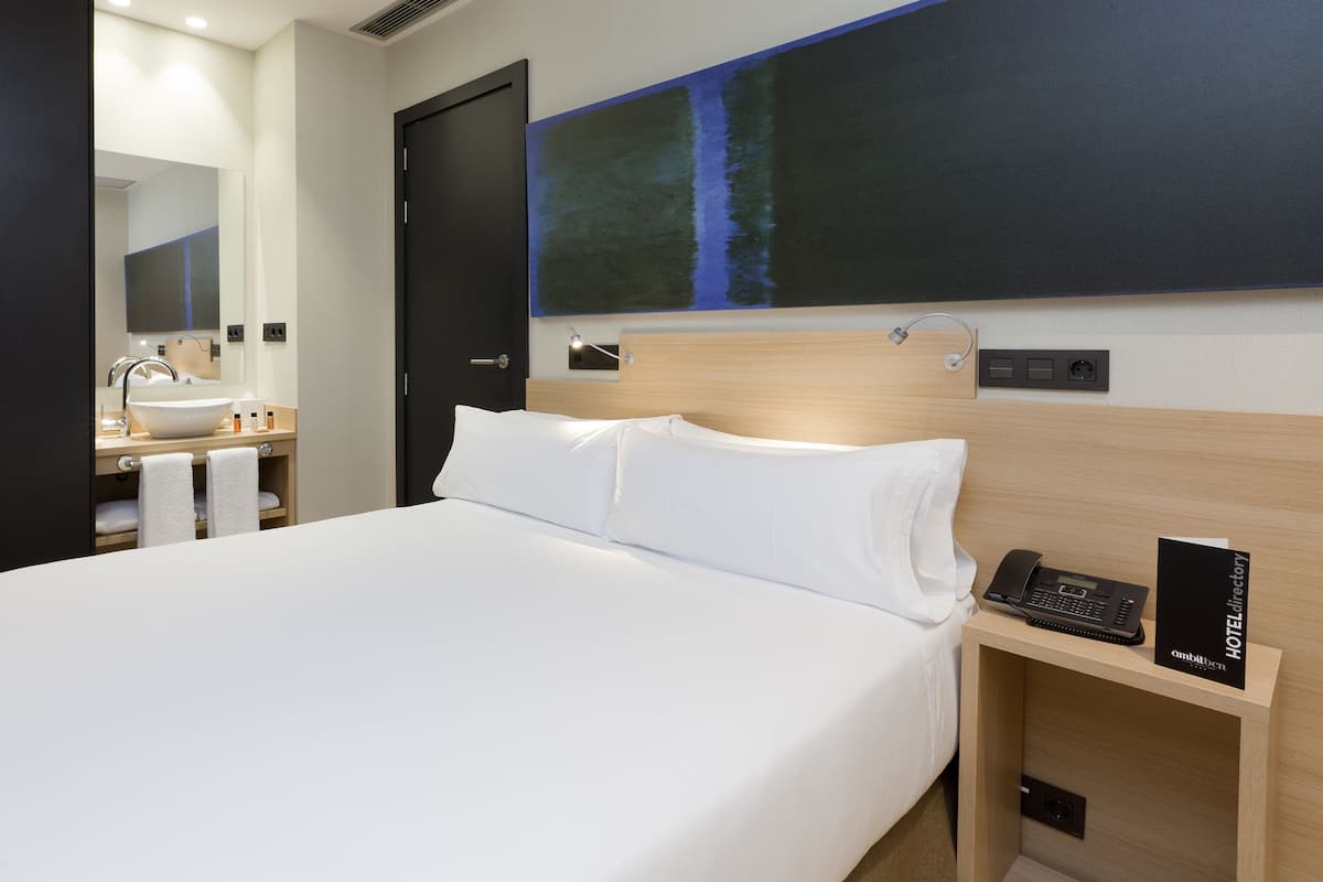 Habitación de hotel con una cama grande, cabecera de madera, teléfono en la mesita de noche y mesita de noche.