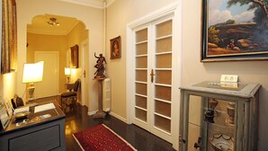 A hallway with a radiator, a desk with a lamp, a chair, and a red rug. - Amica Rome Guest House (Rome)