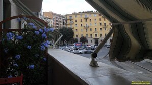 A balcony with a view of a city street, a parked car, and a building with multiple balconies. - Amica Rome Guest House (Rome)