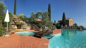 A swimming pool with a wooden bridge, lounge chairs, and a stone wall. - Rigone in Chianti (Montaione)