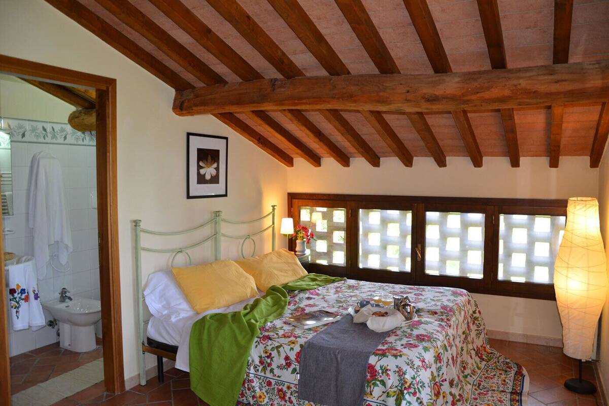 Ein Schlafzimmer mit Bett, Fenster mit Blick, Badezimmer mit Waschbecken und Toilette sowie Holzboden.