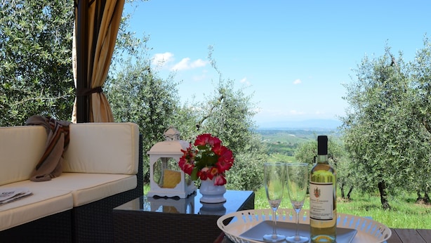 A terrace with a sofa, a table with a bottle of wine, glasses, and a vase with flowers, overlooking a scenic landscape. - Rigone in Chianti (Montaione)