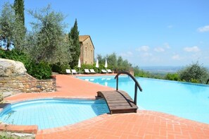 Zona de piscina con muro de piedra, sillas de descanso y vista a un edificio al fondo.