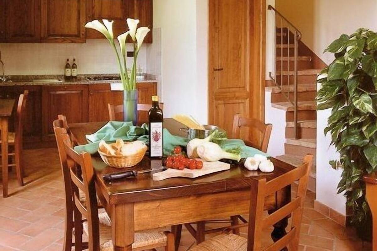 Ein Holztisch mit Stühlen, eine Vase mit weißen Blumen und eine Weinflasche.