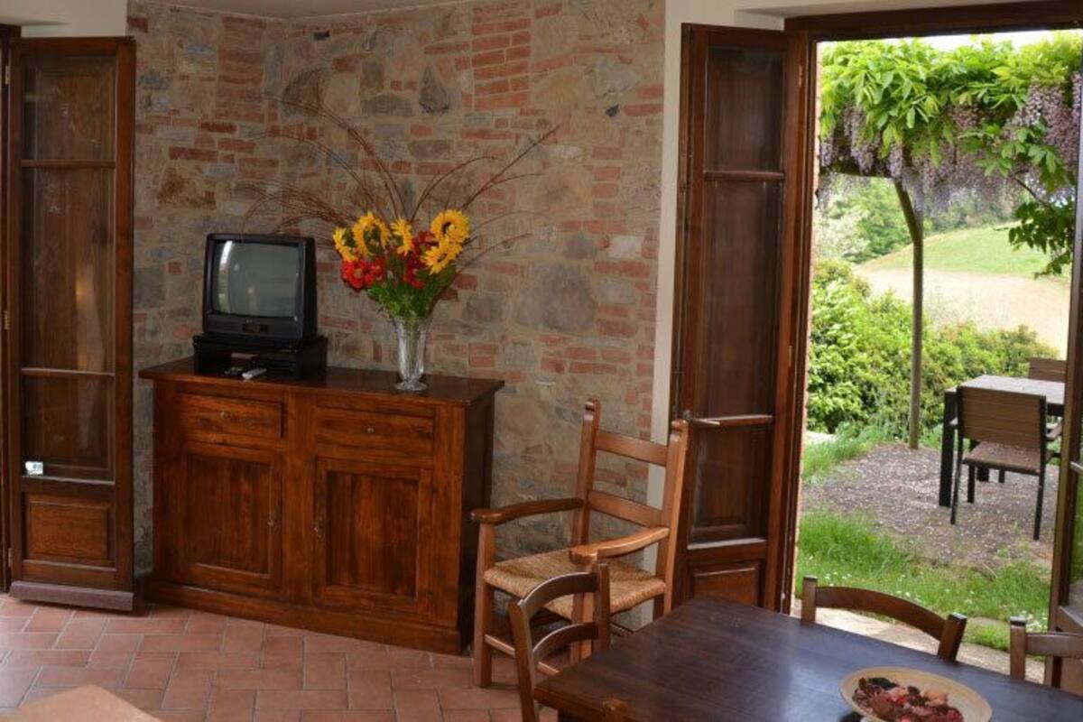 Ein Zimmer mit Backsteinwand, Holzmöbeln, einem Fernseher auf einem Schrank und Blick auf einen Garten.