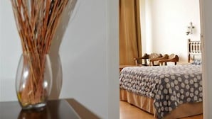 Un dormitorio con una cama, una mesita de noche de madera y un jarrón con plantas secas.