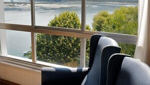 Habitación con un gran ventanal que ofrece vistas a un lago y colinas. Hay dos sillones tapizados en azul oscuro.