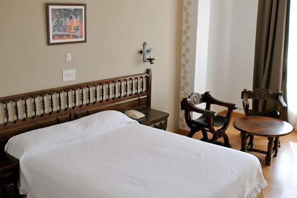 A hotel room with a large bed, a wooden headboard, a small table, two chairs, and a picture on the wall.