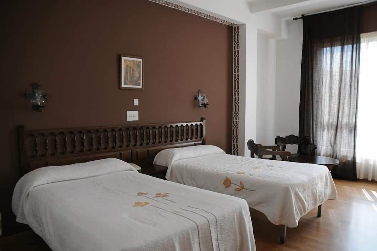 A hotel room with two beds, a wooden headboard, a small table, and a chair.