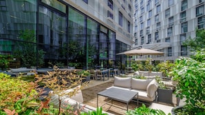 An outdoor seating area with tables, chairs, and a sofa, surrounded by greenery and a modern building facade. - Radisson Blu CDG Airport Terminal Hotel, Paris (Tremblay-en-France)