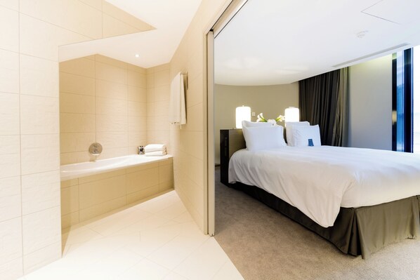 Una habitación de hotel moderna con una cama grande, un baño separado con bañera y vistas a la ciudad desde la ventana.