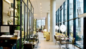 A modern restaurant with glass walls, indoor plants, and a cozy seating area with yellow sofas and tables. - Radisson Blu CDG Airport Terminal Hotel, Paris (Tremblay-en-France)