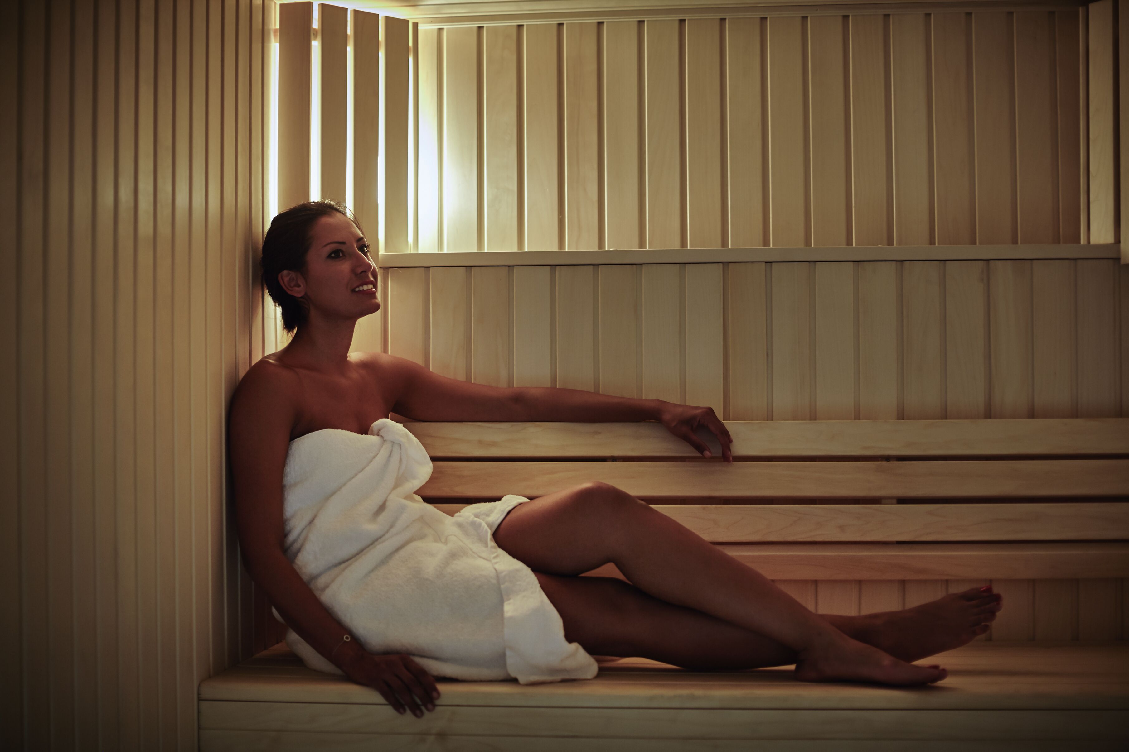 A person sitting in a sauna with wooden benches and slatted walls.