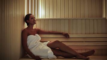 A person sitting in a sauna with wooden benches and slatted walls.