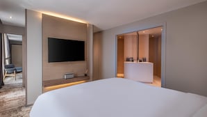 A modern hotel room with a large bed, a flat-screen TV mounted on the wall, a built-in vanity with a mirror, and a separate bathroom visible through an open door. - Radisson Blu CDG Airport Terminal Hotel, Paris (Tremblay-en-France)
