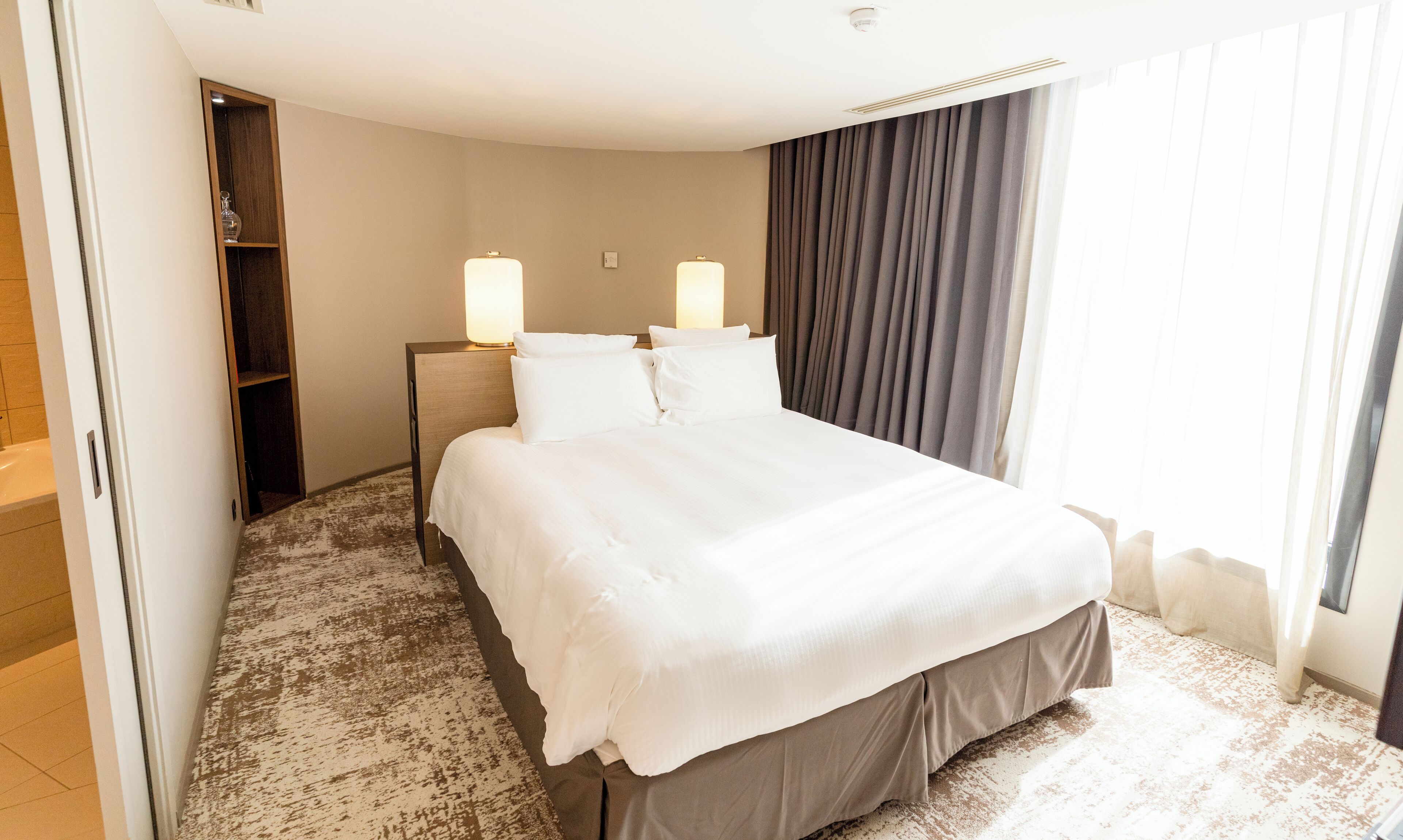 Une chambre d’hôtel avec un grand lit, deux lampes de chevet, une armoire et une vue sur l’extérieur.