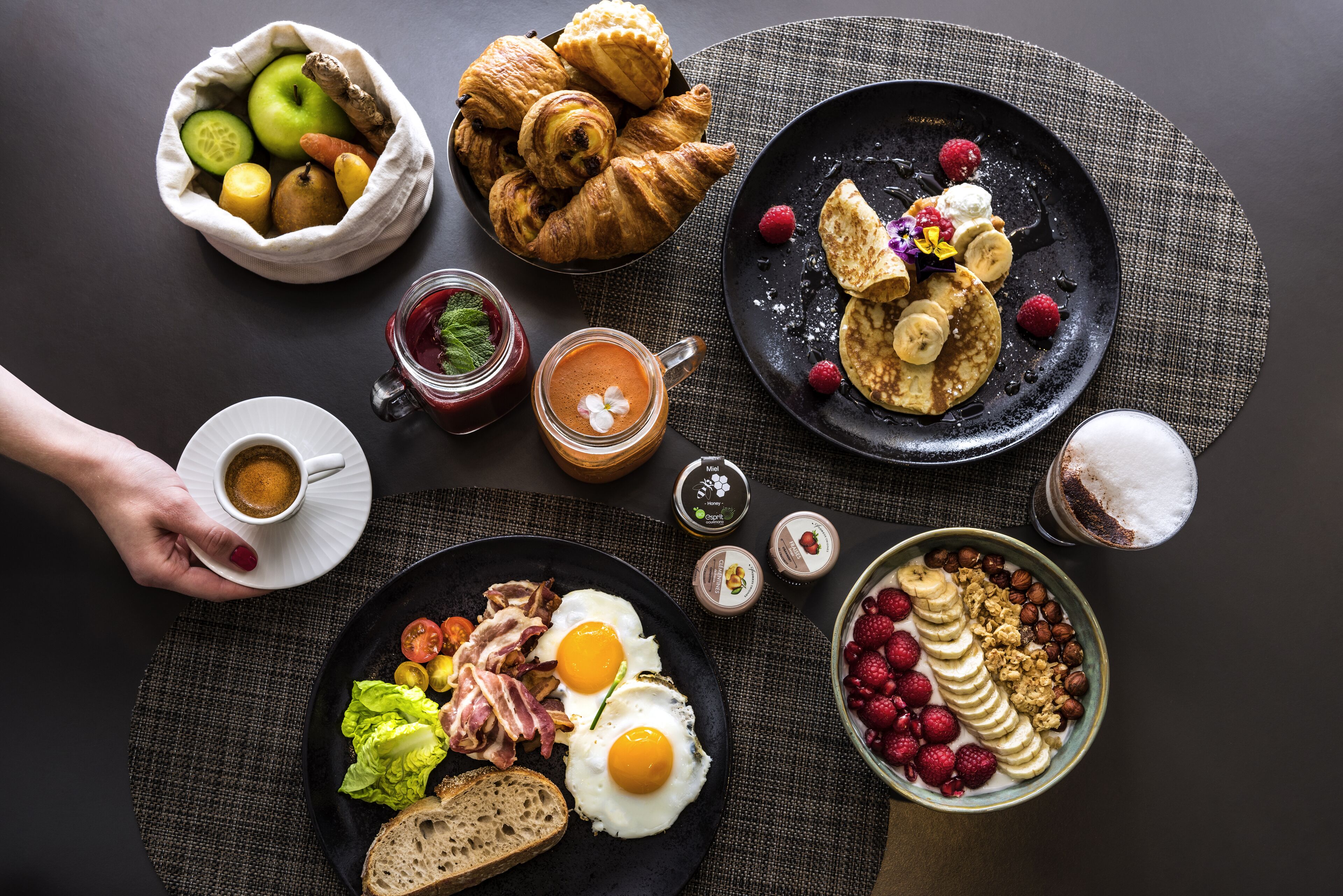 Ein reichhaltiges Frühstücksbuffet mit Croissants, Eiern und verschiedenen Früchten auf einem dunklen Tisch.