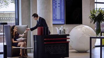 A reception area with a seating area, a black and red cart, a globe decoration, and a digital display board.