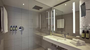 A modern bathroom with a glass-enclosed shower, a large mirror, and a white vanity with toiletries.