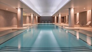 A large indoor swimming pool with a central walkway, surrounded by lounge chairs and columns. - Radisson Blu CDG Airport Terminal Hotel, Paris (Tremblay-en-France)