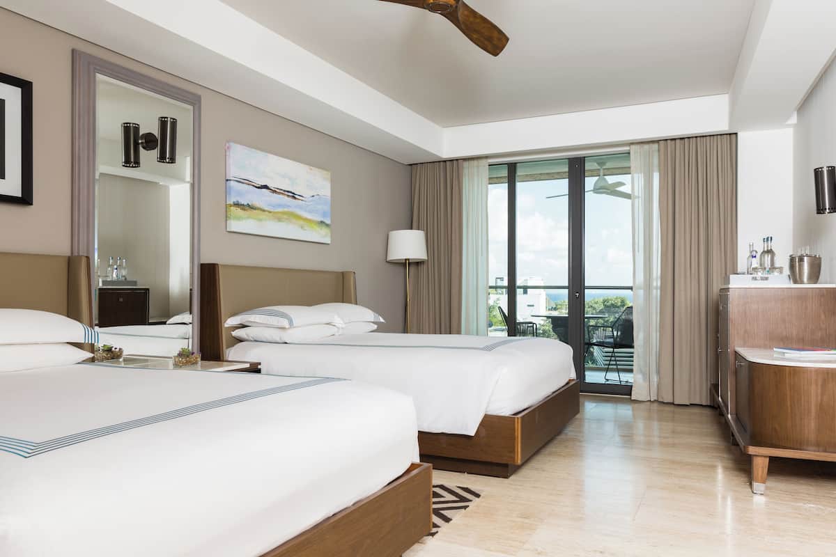Quarto de hotel com duas camas, um espelho grande, um quadro, uma varanda com vista e um aparador de madeira.