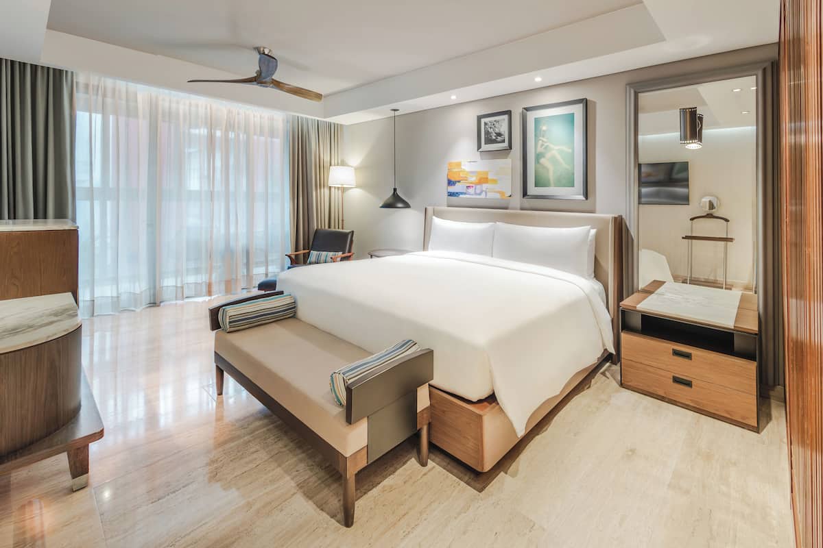 Quarto de hotel moderno com uma cama grande, mesas de cabeceira, uma escrivaninha e vista para a cidade.
